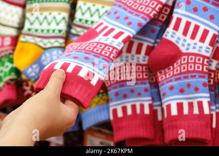 Female hand and warm socks with colorful pattern on a store hangers. Woman choosing outfit and gifts for Christmas holidays Stock Photo