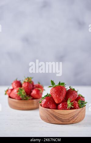 Two wooden bowls with ripe strawberries on a gray background. Vertical, copy space, close-up. Stock Photo