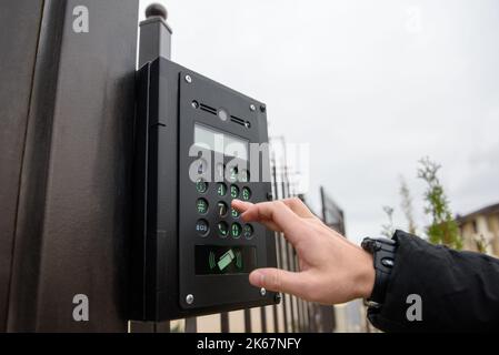 A person's hand reaches for an intercom with camera installed on a street fence. Close-up, copy space. Stock Photo