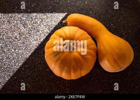 Two pumpkins on a black table surface with light from a window in the shape of a triangle. Autumn concept with copy space. Stock Photo