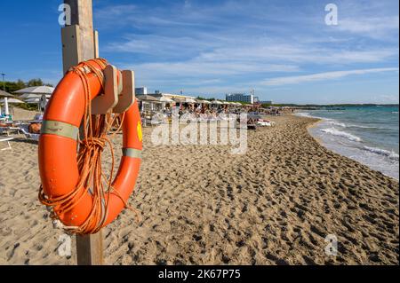 An orange life buoy at the ready in front of sunbathers on Sottovento beach near Gallipoli, Apulia (Puglia), Italy. Stock Photo