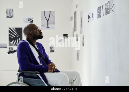 African young man with disability sitting in wheelchair visiting exhibition at art gallery Stock Photo
