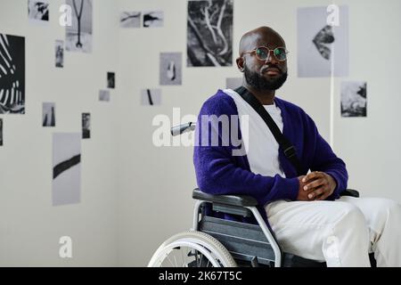 Portrait of African young man in wheelchair looking at camera while visiting art gallery Stock Photo