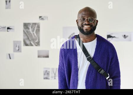 Portrait of African young man in eyeglasses smiling at camera standing at art gallery Stock Photo
