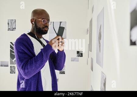 African man in headphones using smartphone while visiting art gallery Stock Photo