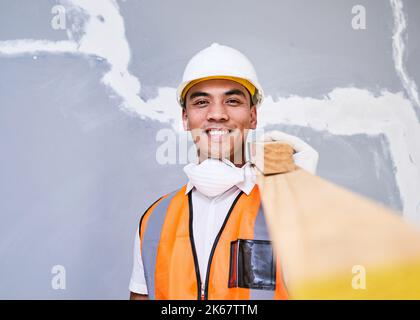 A young Filipino construction worker carries wooden planks on shoulder on site Stock Photo