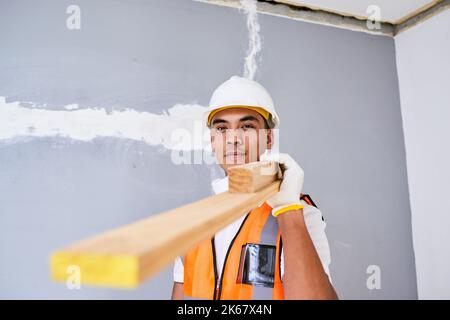 A young Filipino construction worker carries wooden planks on shoulder on site Stock Photo