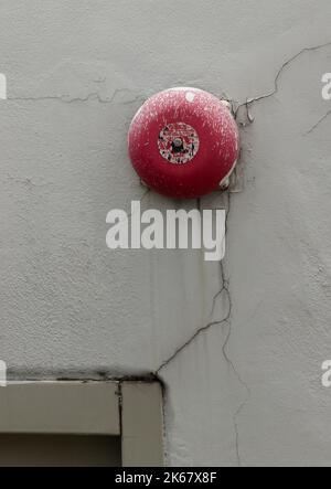 Old and dirty Red fire alarm bell on white concrete wall on top of Emergency fire exit door. Space for text, Selective focus. Stock Photo