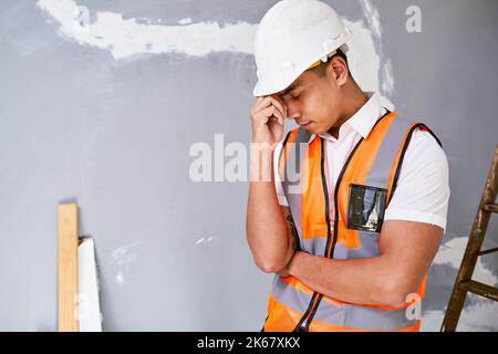 A young Asian construction worker rubs his temples in pain on site Stock Photo