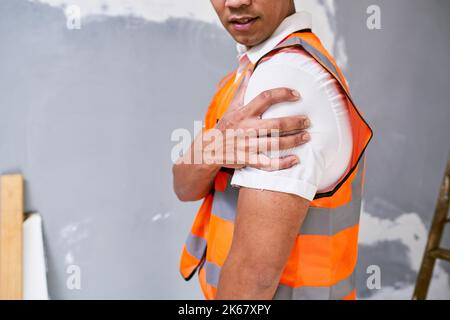 Construction worker holds shoulder in pain from workplace injury on site Stock Photo