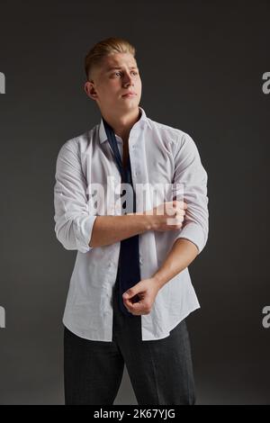 Portrait of young handsome man posing in white shirt isolated over dark grey background. Male fashion collection Stock Photo