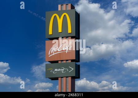 Savigliano, Italy - June 16, 2022: McDonald's sign with McCafe and McDrive logo on blue sky with white clouds. The McDonald's Corporation is world's l Stock Photo