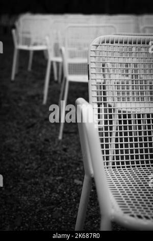 Rows of white metal garden chairs in front of an outdoor stage. Stock Photo