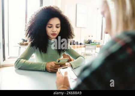 Girlfriends addicted by internet, social network and smartphones technology sitting together and looking at the screen phubbing - people and technolog Stock Photo