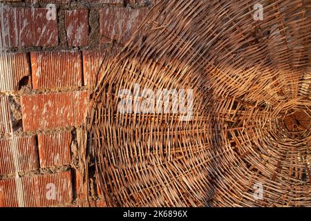straw beach umbrella hat and red brick wall on a summer day, straw beach umbrella. end of tourist season. Stock Photo