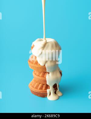 Pouring melted white chocolate over mini bundt cakes. Small bundt cakes stacked on a blue table, traditional Christmas dessert. Stock Photo