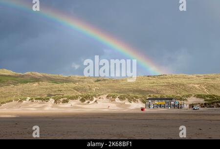 Cornish rainbow landing on Sand dunes at Perranporth, above beach Cafe Stock Photo