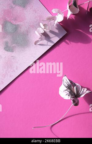 Abstract flat lay with dry cala lily flower and eucalyptus twig painted metallic pink. Layered vibrant magenta and metallic pink silver paper. Stock Photo
