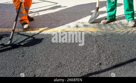 The road workers' working group updates part of the road with fresh hot asphalt and smoothes it for repair. Stock Photo