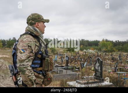 Lyman, Ukraine. 11th Oct, 2022. A Ukrainian soldier was seen standing in a cemetery in Lyman. A burial site was discovered next to the cemetery by the Ukrainians after the city was liberated from Russian troops in Donetsk region. At least 32 Ukrainian soldiers' bodies have been exhumed from a mass grave in Lyman, a city in Donetsk region that was under Russian occupation. Authorities said they were buried together and initial investigation has shown some bodies were blindfolded and tied on the hands, which suggested signs of torture and execution. Another 22 civilians, including children w Stock Photo