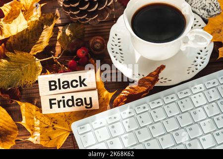 Wooden block with the words Black friday, Autumn leaves, white computer keyboard, cup of coffee, Concept, Searching for promotions and seasonal sales Stock Photo