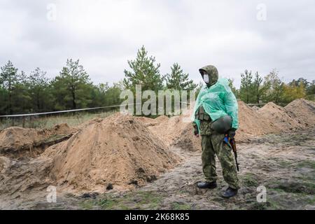 Lyman, Ukraine. 11th Oct, 2022. A Ukrainian soldier is seen standing next to a burial site where soldiersÃ- bodies were exhumed. At least 32 Ukrainian soldiers' bodies have been exhumed from a mass grave in Lyman, a city in Donetsk region that was under Russian occupation. Authorities said they were buried together and initial investigation has shown some bodies were blindfolded and tied on the hands, which suggested signs of torture and execution. Another 22 civilians, including children were exhumed from another burial site nearby. Both sites located at the edge of a cemetery. Officials Stock Photo