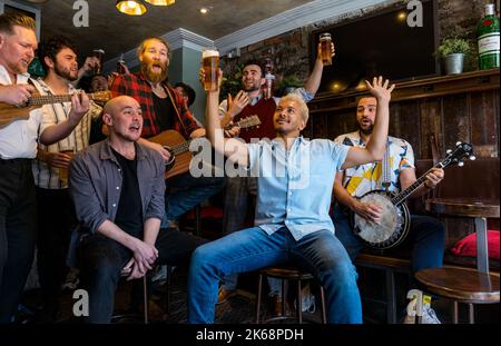 Choir of Man group singing, playing music and drinking beer in a pub, Grassmarket, Edinburgh, Scotland, UK Stock Photo