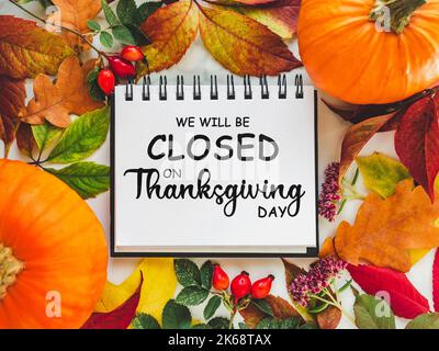 We will be closed for the Holidays. Beautiful Thanksgiving sign. Bright pumpkins, tree leaves, red berries and colorful flowers lying on an empty tabl Stock Photo