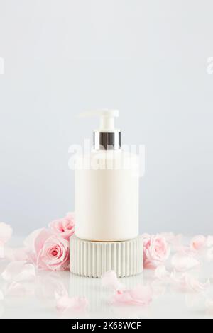 Dispenser white bottle on marble podium with tender pink roses Stock Photo