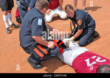 softball Player with broken leg is attended to by fire personal and wife as team members look on while laying on ball field during softball game Stock Photo