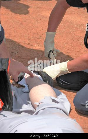 softball Player with broken leg is attended to by fire personal and wife as team members look on while laying on ball field during softball game Stock Photo