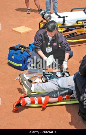 softball Player with broken leg is attended to by fire personal and wife as team members look on while laying on ball field during softball game Stock Photo