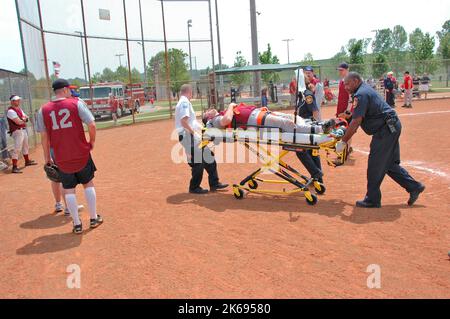 softball Player with broken leg is attended to by fire personal and wife as team members look on while laying on ball field during softball game Stock Photo