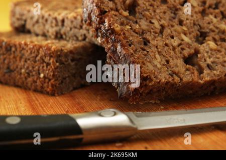 Sliced whole grain bread with a knife on a wooden board. Defocus. Healthy food concept. Stock Photo