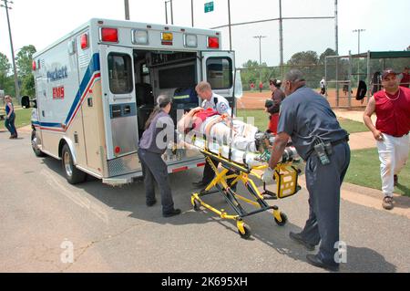 softball Player with broken leg is attended to by fire personal and wife as team members look on while laying on ball field during softball game Stock Photo