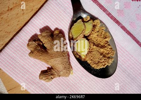 Ginger root and spoon with ginger slices and powder on cotton napkin on wooden trencher. Pungent healthy asian spice. Top view closeup. Stock Photo