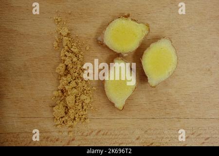 Ginger slices and powder on wooden trencher. Top view closeup. Stock Photo