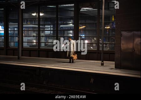 07.10.2022, Berlin, Germany, Europe - A man looks at his mobile phone as he waits for the train on a platform at Bahnhof Zoologischer Garten station. Stock Photo