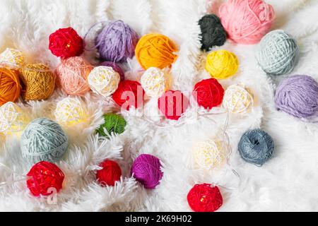 Bright multicolored knitting yarn and a luminous garland in the form of balls lie on fluffy blanket. Stock Photo