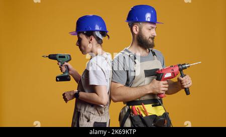 Team of engineers using power drill machine to screw nails and work on construction redevelopment in studio. Builders working with electric drilling nail gun on industrial demolition. Stock Photo