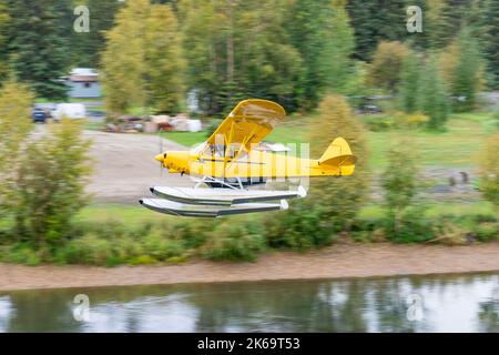 Yellow bush float plane flying over river in Alaska Stock Photo