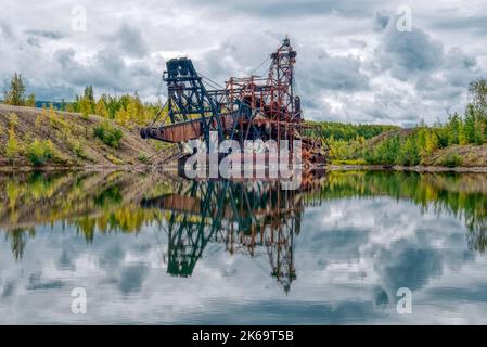 Old rusty abandoned gold mining dredge in a pond in Alaska Stock Photo