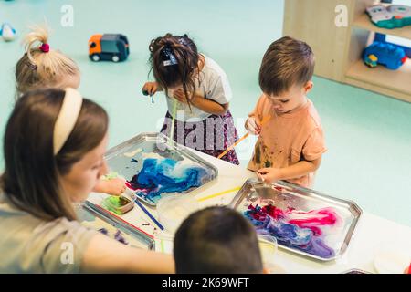 cute preschoolers enjoying with water paints with their teacher in kindergarten. High quality photo Stock Photo