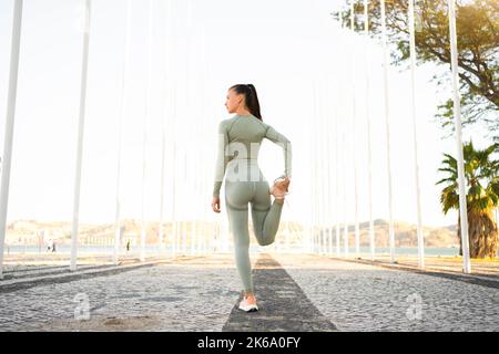 Woman Stretching And Warming-Up Legs Before Running. Fit sport woman stretching her body warm up before workout outdoor. Girl in sportswear exercises outside in summer park for health and wellbeing. Stock Photo