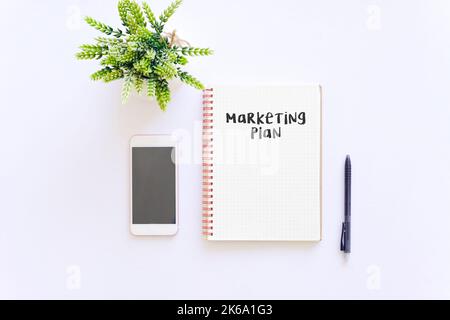 Business concept : Marketing plan word on notepad with smartphone and green plant, isolated white background Stock Photo
