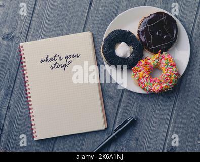 Top view of Notebook, ballpen, and doughnut on wooden background with WHAT'S YOUR STORY word Stock Photo