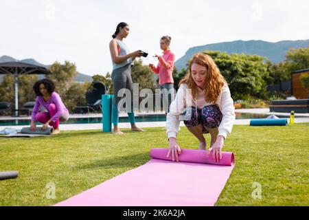 Diverse friends talking and rolling yoga mats in garden Stock Photo