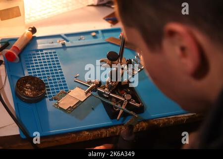 Defocus man with microscope. Work with a soldering iron. Microelectronics device. Close-up hands of a service worker repairing modern smartphone. Repa Stock Photo