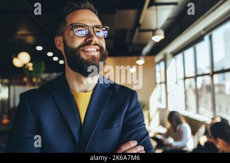 businessman thinking of new business ideas in a co-working space. Thoughtful businessman smiling cheerfully while standing with his arms crossed. Youn Stock Photo