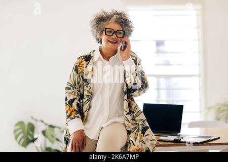 Cheerful businesswoman smiling happily while speaking with her business partners on a phone call. Mature businesswoman making business plans while sit Stock Photo
